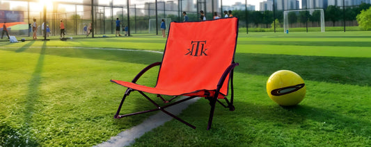 Silla de playa plegable naranja KTK Kontiki colocada junto a un campo de fútbol infantil, ideal para ver deportes infantiles al aire libre 