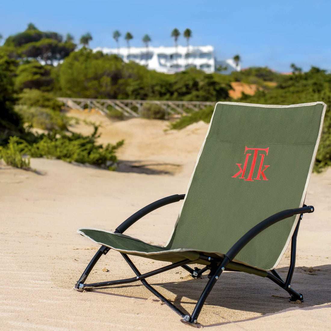 Silla de playa verde KTK KONTIKI plegable y portátil sobre arena en la costa española, diseño ergonómico premium para mujeres modernas.