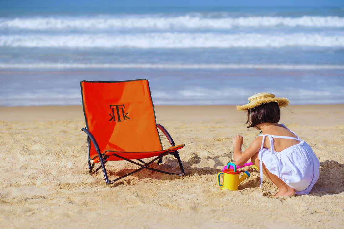 Silla de playa plegable naranja KTK Kontiki junto a una niña jugando en la arena, en una playa familiar y soleada de España