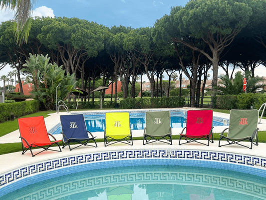 Sillas de playa plegables KTK Kontiki de colores variados alineadas junto a una piscina en un entorno natural con pinos, ideales para disfrutar con estilo del verano en jardines o playas.