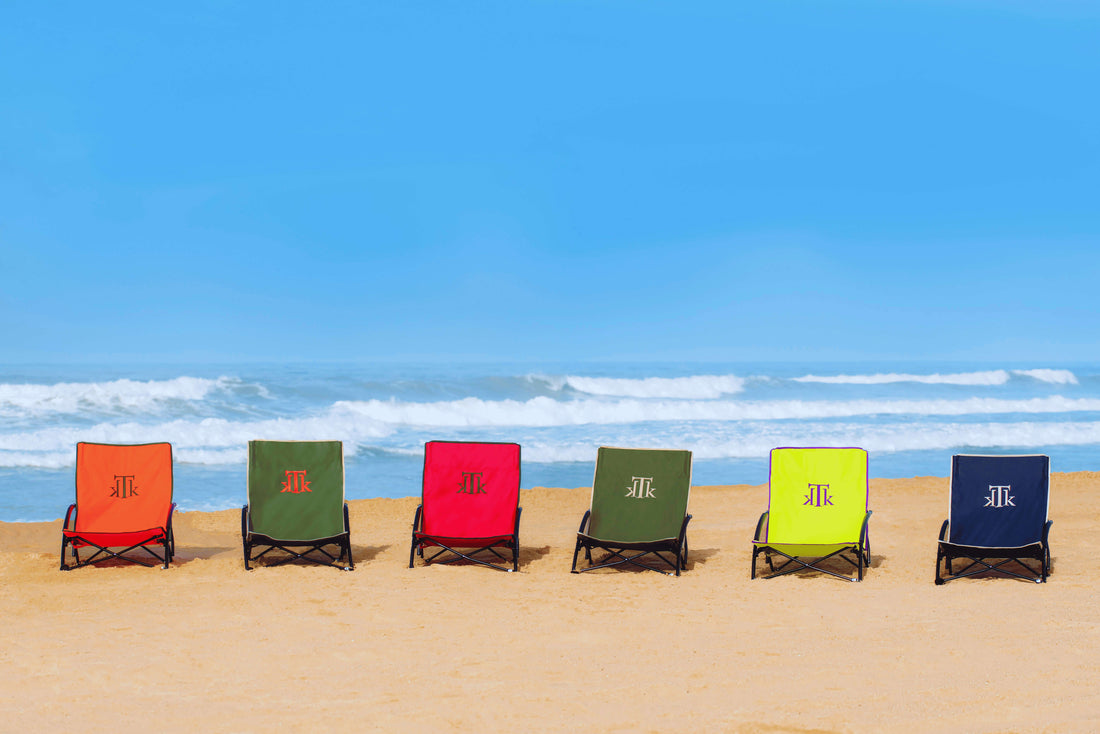 Sillas de playa plegables KTK Kontiki en colores vibrantes alineadas sobre la arena frente al mar, diseño low profile, estructura de acero reforzado y bolsa de transporte, ideales para playa, picnic y festivales de verano.