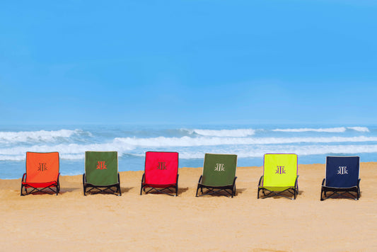 Sillas de playa plegables KTK Kontiki en colores vibrantes alineadas sobre la arena frente al mar, diseño low profile, estructura de acero reforzado y bolsa de transporte, ideales para playa, picnic y festivales de verano.